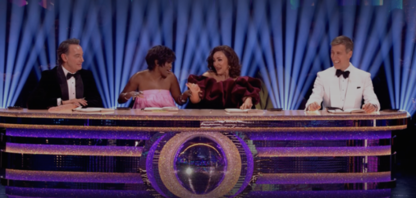 Four judges, two men and two women, sit behind a glittery desk.