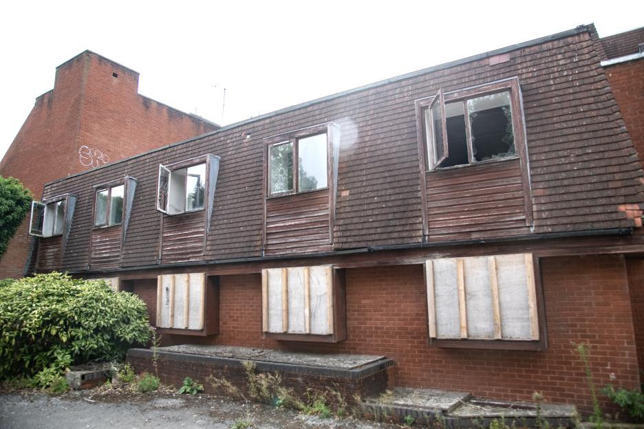 Derelict building with boarded-up and broken windows.