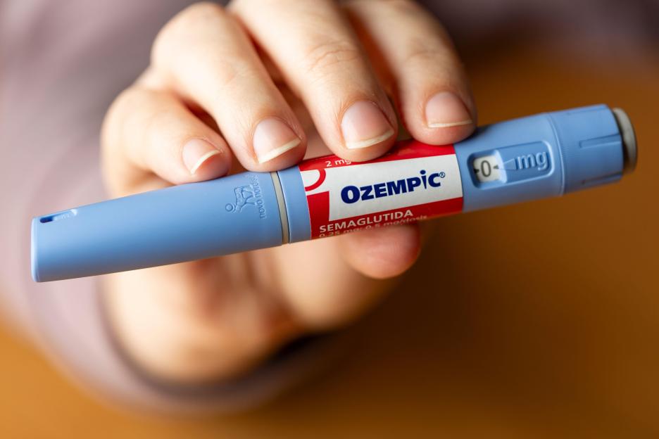 A hand holds a blue and red Ozempic pen injection with "0 mg" displayed.