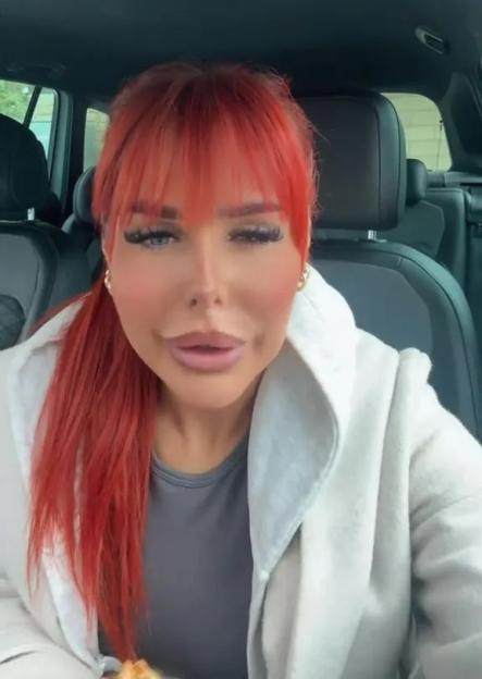 A woman with red hair and heavy makeup sitting in a car.