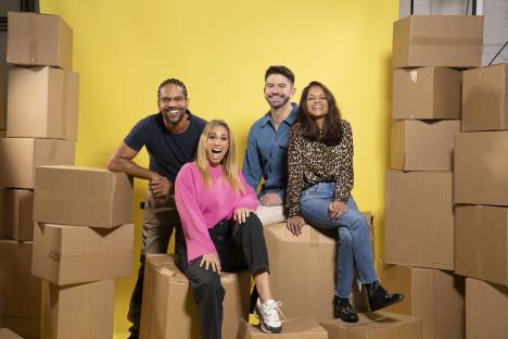 Four people smiling and sitting on cardboard boxes.