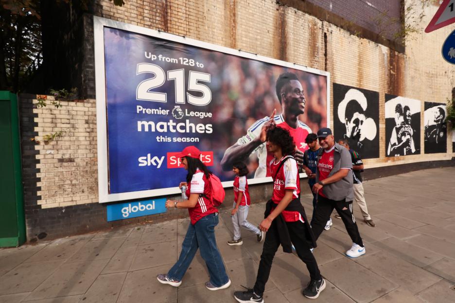Arsenal fans walk past a Sky Sports advertisement featuring Bukayo Saka.