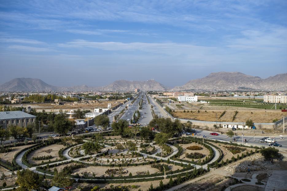 Aerial view of Kabul, Afghanistan, with a long highway stretching into the distance and mountains in the background.