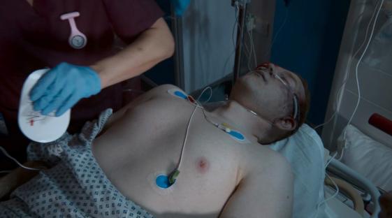 A nurse prepares to use a defibrillator on a patient in a hospital bed.
