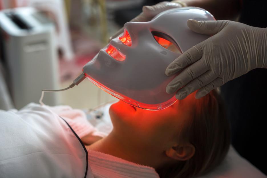 Woman receiving LED light therapy facial treatment.
