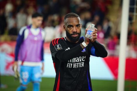 Alexandre Lacazette, wearing a black jersey, holds a water bottle and acknowledges the crowd.