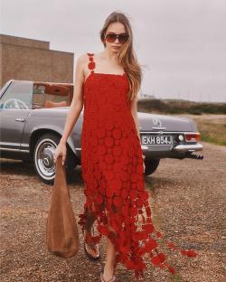 Woman in red dress and sunglasses walking near a vintage car.