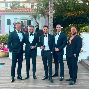 Five men in black tuxedos at an outdoor event.