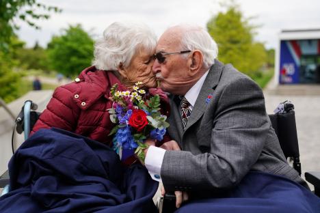A 101-year-old couple kissing, holding a bouquet of flowers.