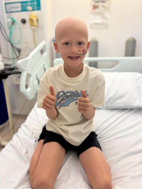 Tommy Verbickas, a young child with cancer, giving two thumbs up in a hospital bed.