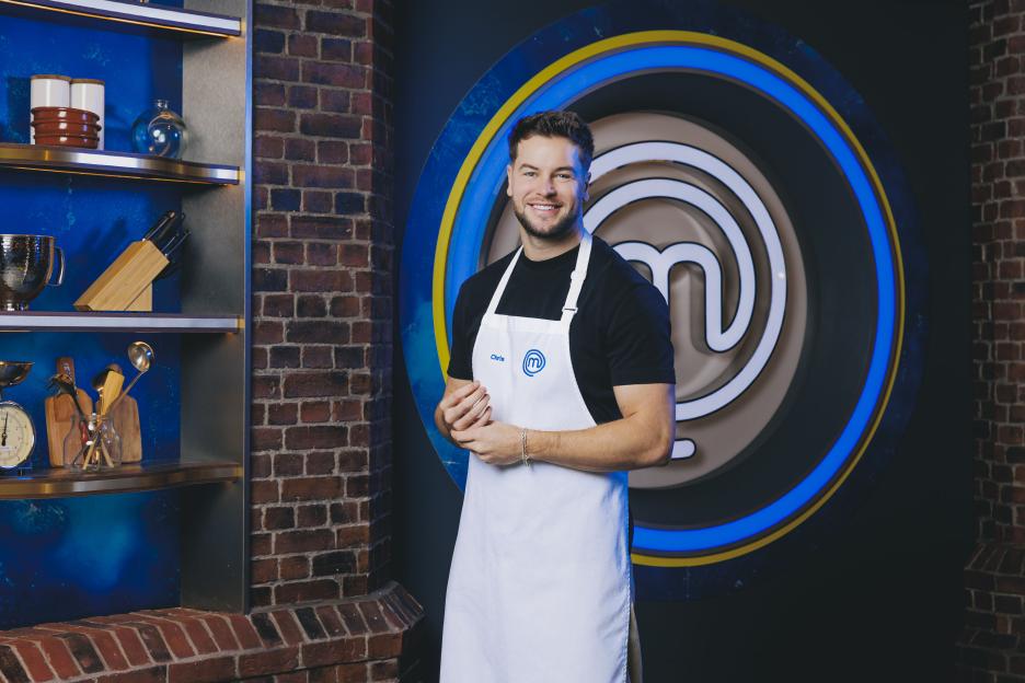 Chris in a white MasterChef apron stands in a kitchen setting.