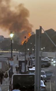 Wildfire engulfing a cliff above a beach.