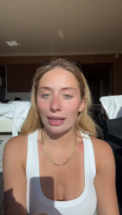 Woman in white tank top speaking to camera.
