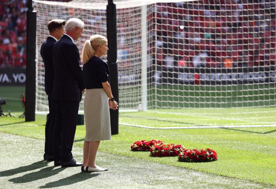 Three people laying wreaths at a soccer field.