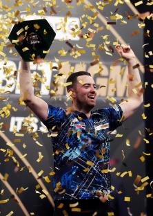Luke Humphries celebrating a darts victory, holding a trophy aloft amidst confetti.