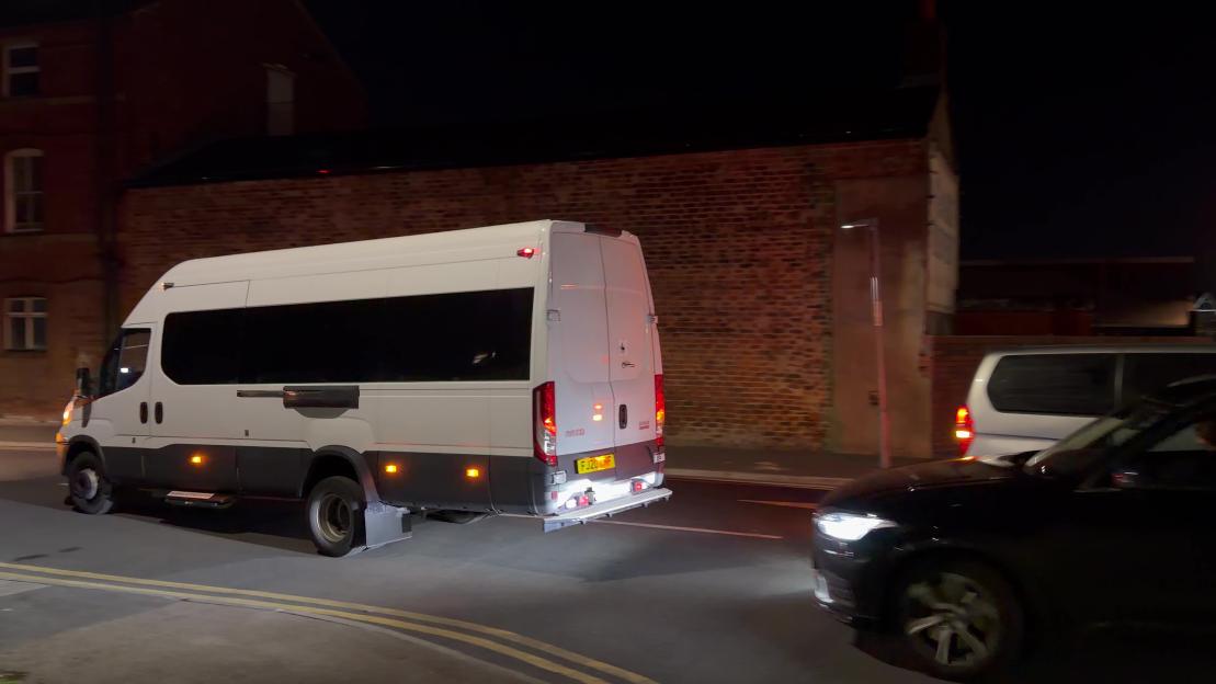 A white prison van driving on a street at night.