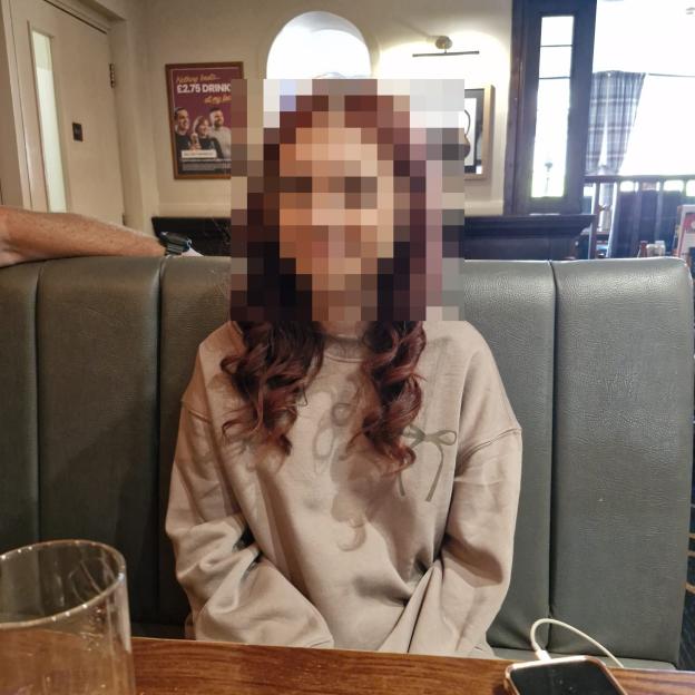 A young girl, 15, sitting at a booth, with her face pixelated.