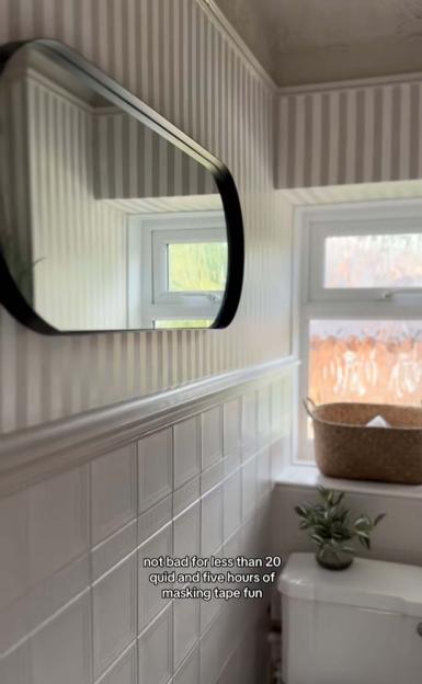 DIY bathroom renovation with striped walls above a white tiled wainscot, including a mirror and window.