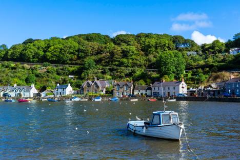 Small boat in harbor with village houses and green hillside in background.