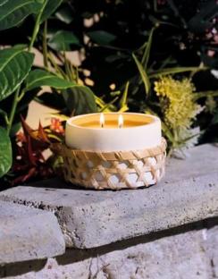 A lit citronella candle in a woven basket, sitting on a stone wall.