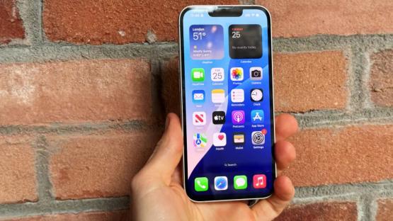 Hand holding iPhone displaying apps and widgets.
