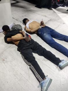 Handcuffed people lying on the floor surrounded by armed police.