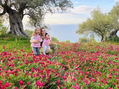 Family with two young children sitting in a field of flowers near the ocean.