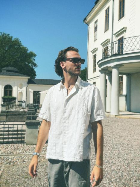 Man in sunglasses and white shirt standing outside a large white building.