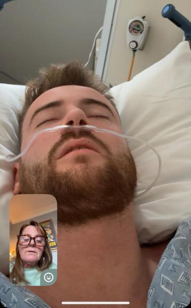 A man with a nasal cannula in a hospital bed on a video call.