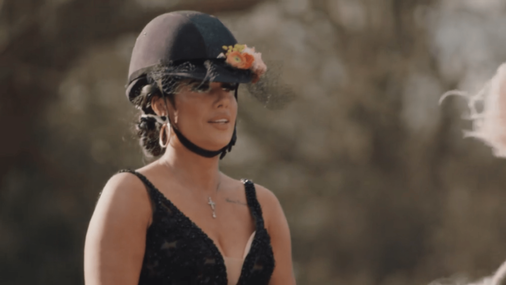 A woman with an equestrian helmet adorned with flowers and a black dress.