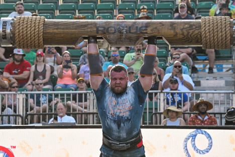 A strongman competitor overhead pressing a heavy log at the World's Strongest Man competition.