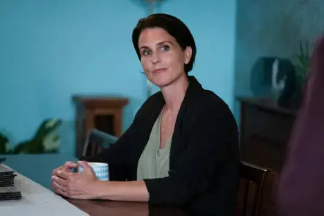 Woman sitting at a table, holding a mug.