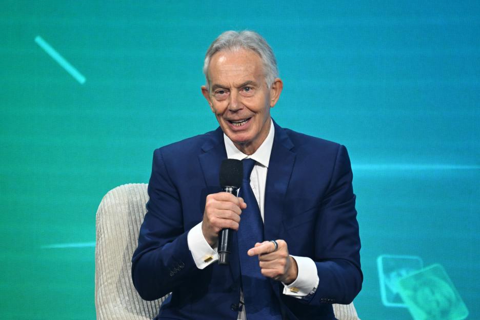 Tony Blair speaking into a microphone while sitting in a chair.
