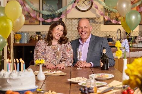 Kirstie Allsopp and Phil Spencer at a table with food and champagne, celebrating.