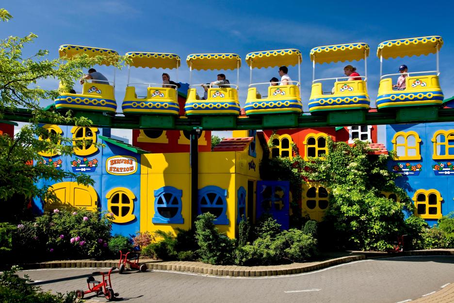 The Lego train at Legoland park with passengers on the monorail over colorful buildings.