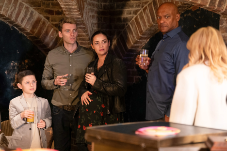 A group of people, including a pregnant woman and a child, standing in a dimly lit room.