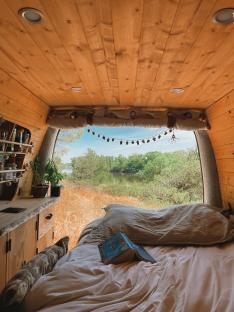Interior of a converted van with a bed and a view of a lake.