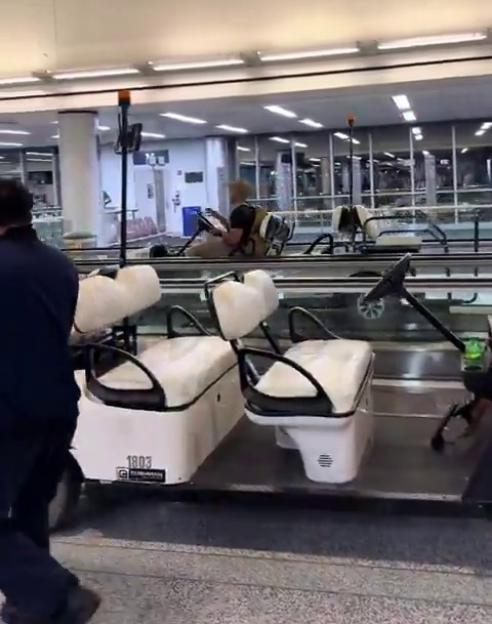 Person driving a golf cart on a moving walkway in an airport terminal.