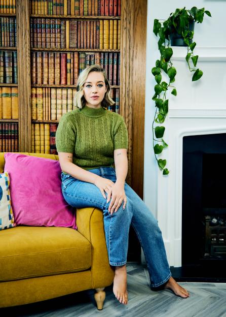 Kelsey Parker sitting on a yellow sofa with bookshelves in the background.