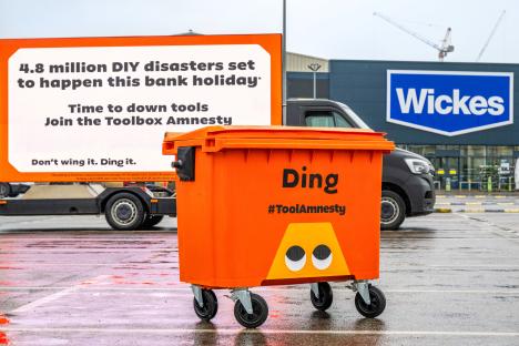 Orange #ToolAmnesty bin in parking lot with billboard advertising the campaign.