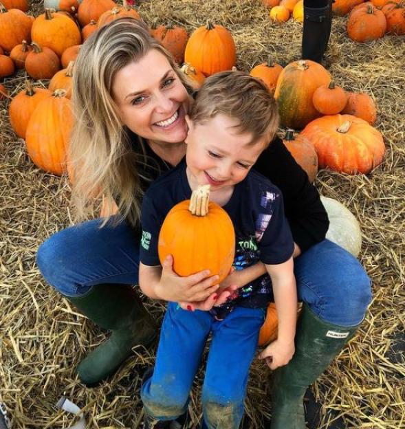 Woman and young child smiling with pumpkins.