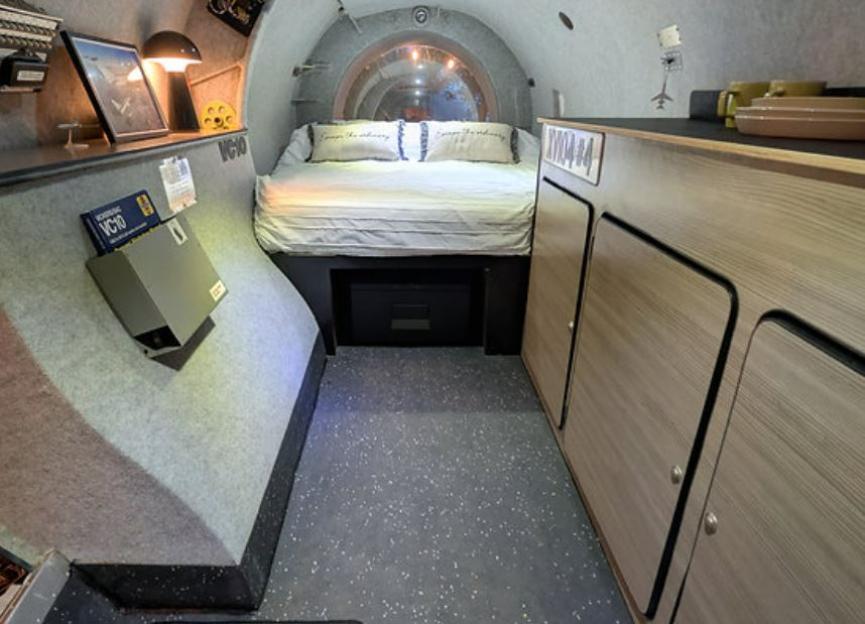 Interior of a Rolls Royce engine pod glamping unit with a bed and storage.