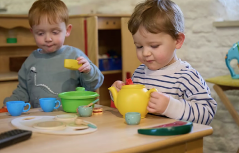 Two toddlers playing with a toy tea set.