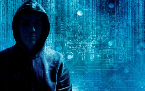 Hooded hacker in front of a circuit board background.