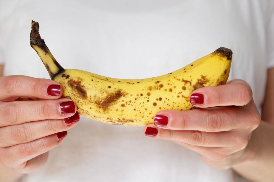 Person holding a ripe banana with brown spots.