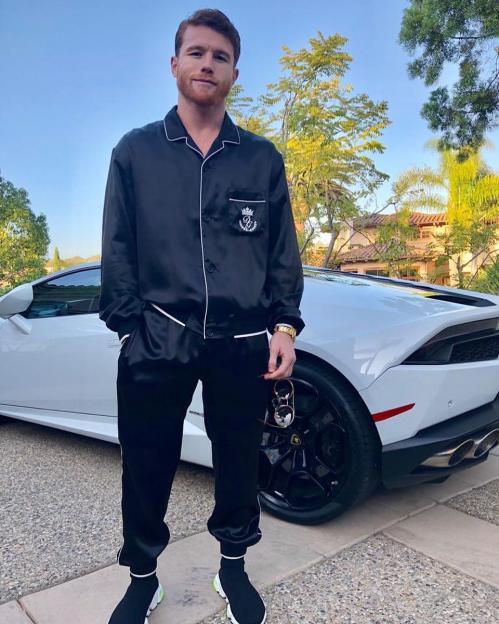 Canelo Álvarez standing by a white Lamborghini.