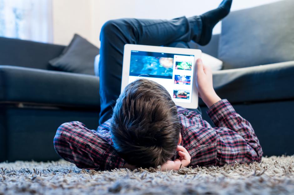 Teenager lying on the floor using a tablet.