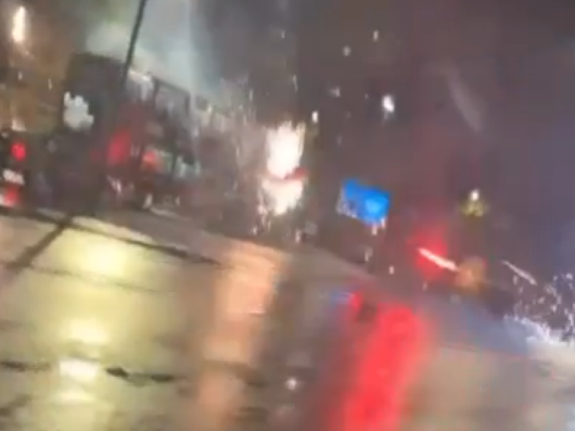 A bus driving through heavy rain at night, seen through a wet windshield.