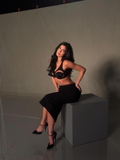 Woman in black lingerie and skirt sitting on a cube.