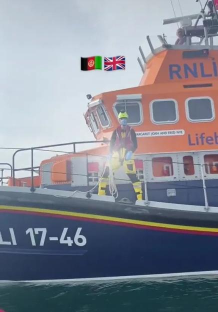 A person in a life jacket and yellow protective gear stands on a lifeboat with the text "RNLI 17-46" and flags of Afghanistan and the UK superimposed.